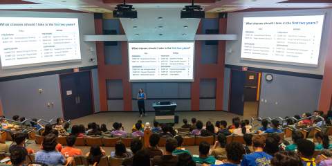 A photo of an advisor speaking to a group of new students in a lecture hall.