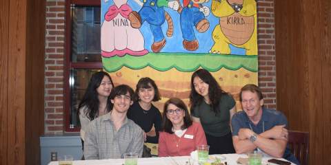 A group of students and teachers posing at a table in front of a Mario themed banner 