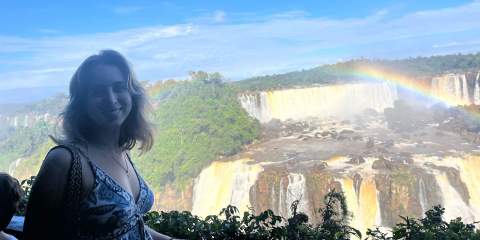 A girl posing in front of a waterfall with a rainbow 