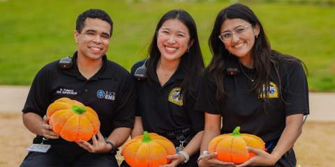 3 rice students holding pumpkins and sitting on a hay bale posing for a photo 