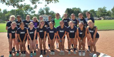 A team of women posing in a sports field wearing matching navy uniforms 