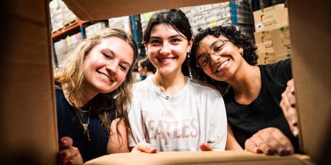 3 college students looking through an open cardboard box at the camera
