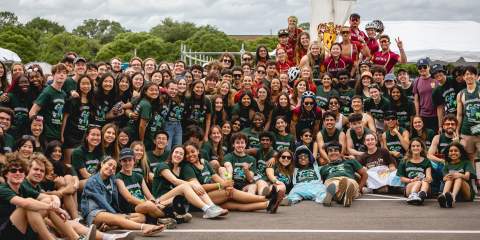 A very large group of college students posing for a photo in a parking lot 