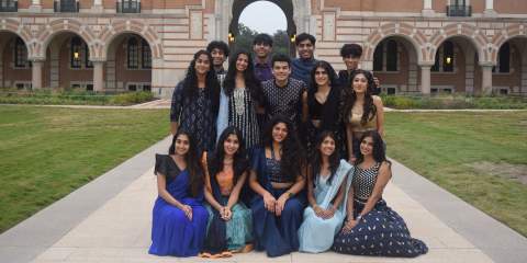 College students posing as a small group in front of a large arch 