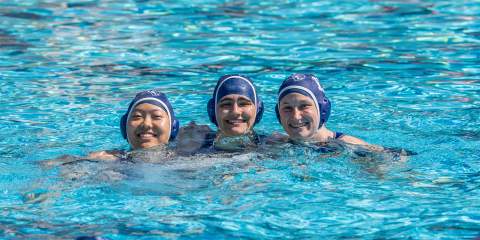 A photo of three Rice students smiling at a women's club water polo match.