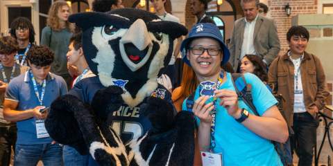 A Rice student posing with the Rice Owl mascot Sammy