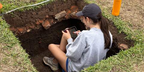 Girl sitting inside square hole dug in the grass