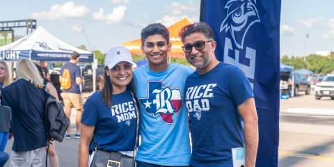 A young guy and his parents standing together in front of a parking lot and banner