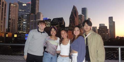 Five people standing in front of a skyline at dusk