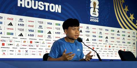 A guy sitting in a broadcasting booth, with several sponsor and FIFA World Cup logos behind him