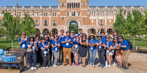 Large group photo of people in matching blue shirts in front of a building