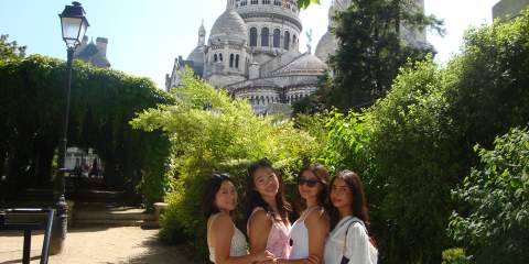 Four girls standing in front of trees and an ornate building