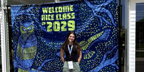 A girl standing in front of a vivid, blue banner with the text "Welcome Class of 2029"