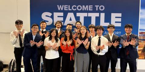 Large group of people in business formal attire standing in front of a sign that says "Welcome to Seattle" in white block letters