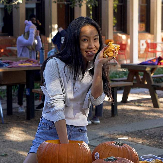 A Rice student smiles and holds up part of the pumpkin that she's carving.