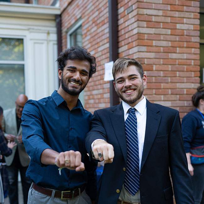 Two male Rice students fist bump the camera to show off their new Rice rings.