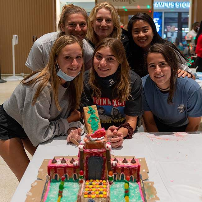 A group of six women students smile in front of the gingerbread house they made, which looks like Lovett Hall.