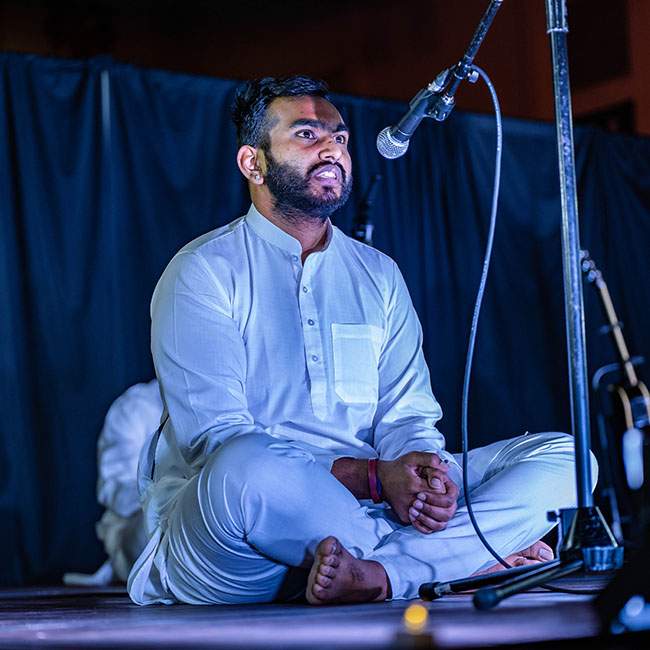 A student sitting on the floor singing as part of the group Aag at Dhamaka.
