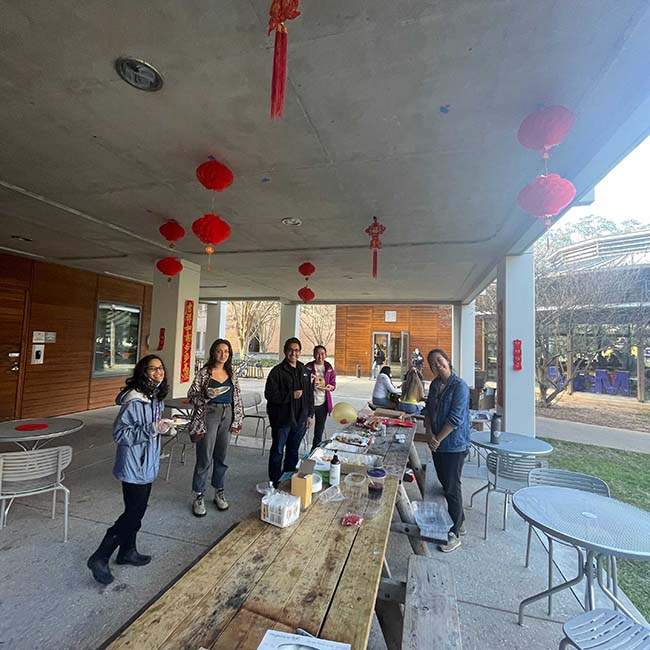 A picture taken from farther back of a group of students standing in front of a table with food for a Chinese New Year celebration.