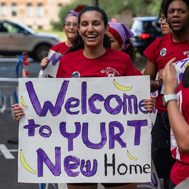 A current Rice student at O-Week holds up a sign that says "Welcome to Yurt New Home" to welcome new students to Rice University.