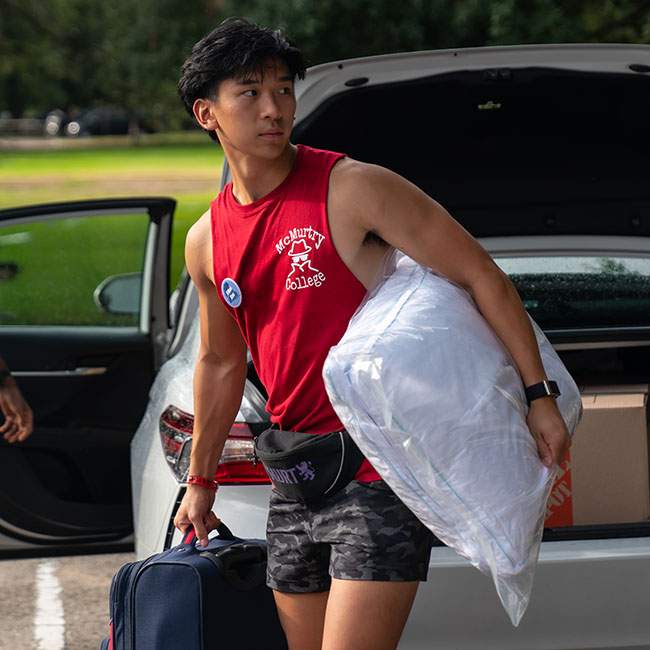 A current Rice student carries a pillow and a suitcase to help a new student move into their residential college.