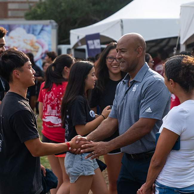On the right hand side of the picture, President DesRoches shakes the hand of a new student greeting him in the middle of a large crowd of students.