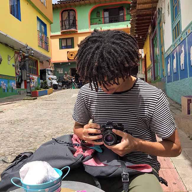 The picture shows Arinze, a Rice student, sitting on a street in Columbia, looking down at his camera.