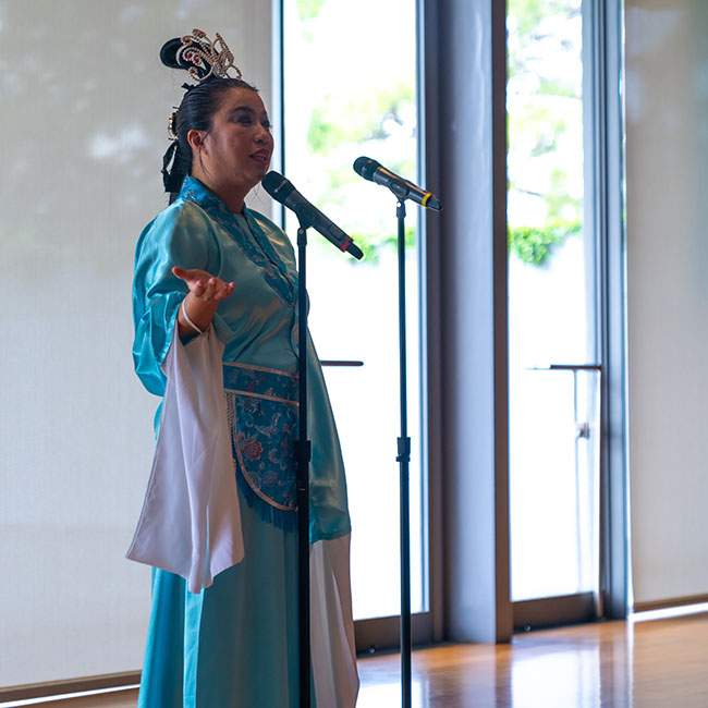 A woman from the Asia Society wearing a blue piece of traditional Chinese clothing called a hanfu introduces the performances for the festival.