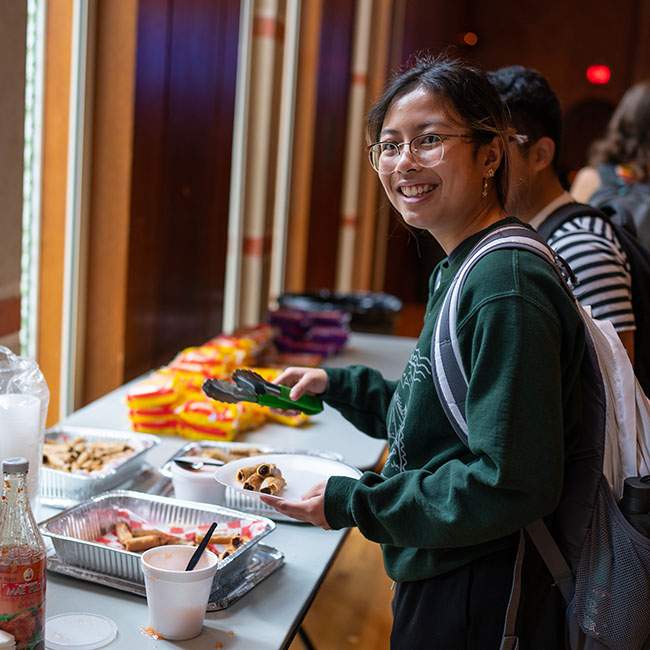 A Rice student smiles for a picture while holding a plate of Filipino food.