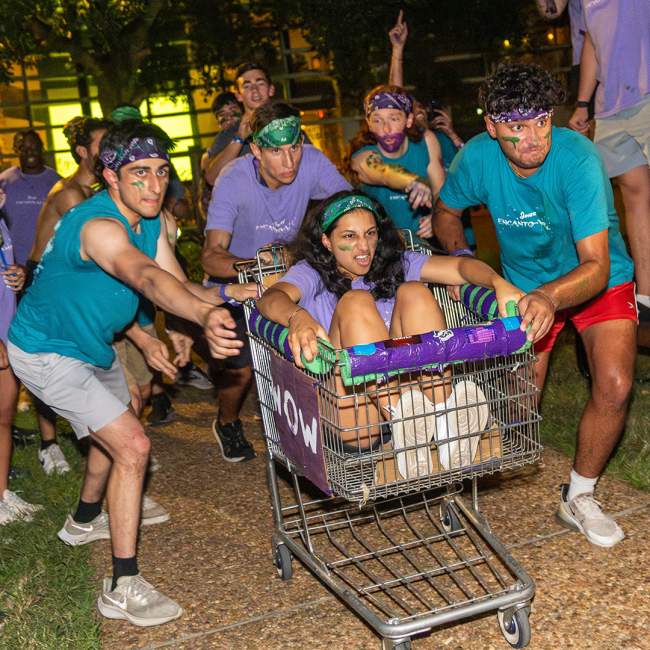 a student rides a shopping cart while other students push the cart