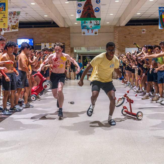 Two students racing each with a tricycle in hand