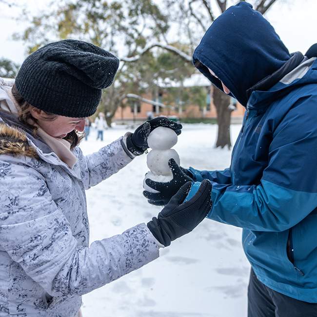 Two college students making a snowman in their hands