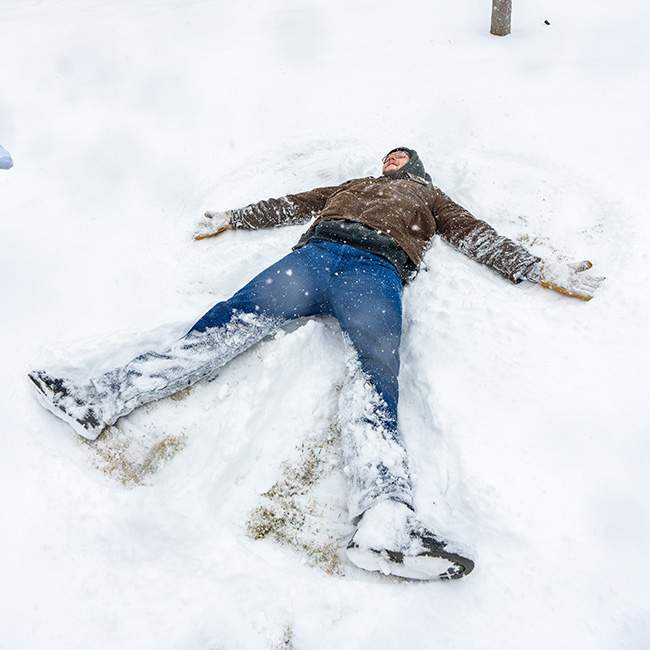 A person in a brown coat and jeans making a snow angel 