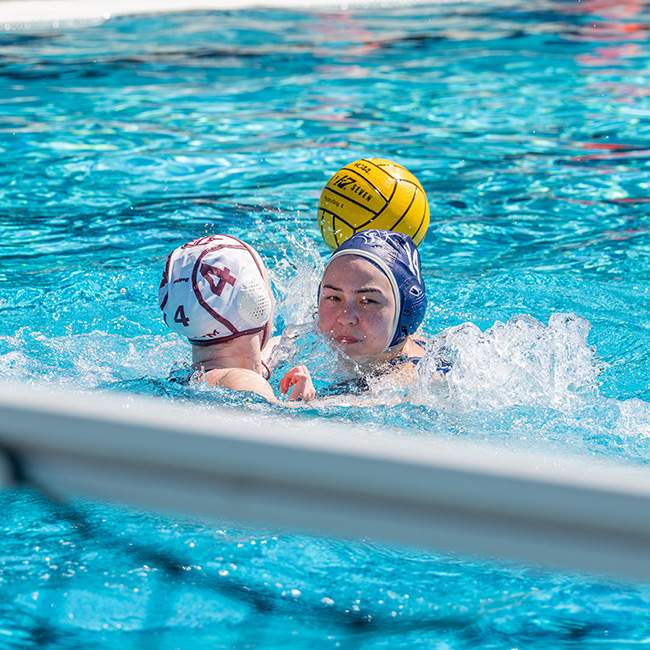 A girl attempting to score a goal in water polo being blocked by another player 