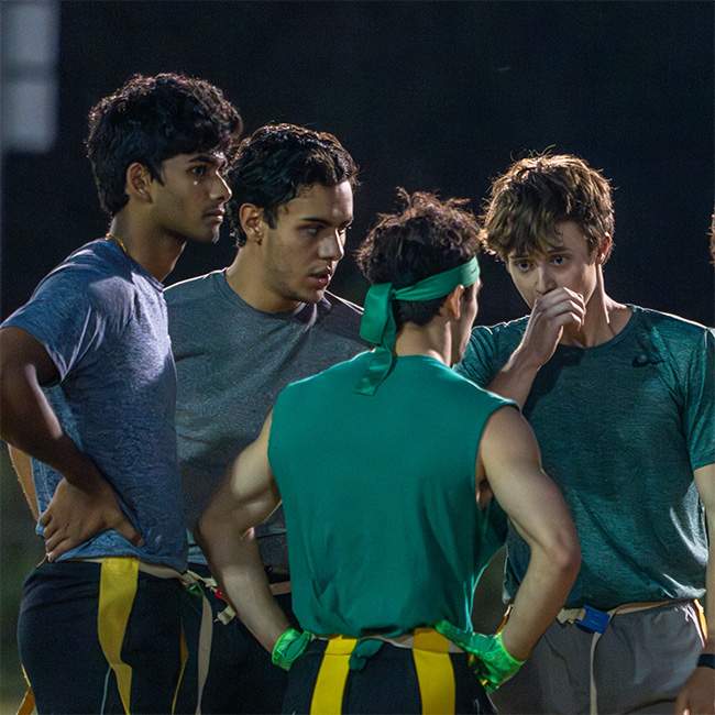 A group of photos in athletic clothing huddle together in discussion.