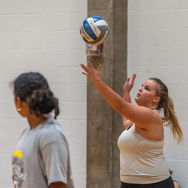 A girl reaches out to hit a volleyball in midair