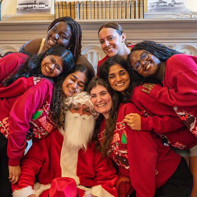Many girls huddled together around a peer in a Santa Claus costume