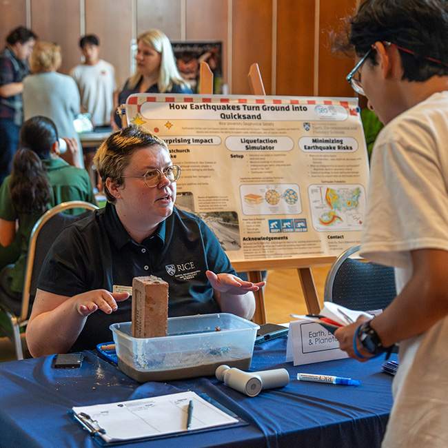 A person behind a table showing a display sitting on a table to a student watching