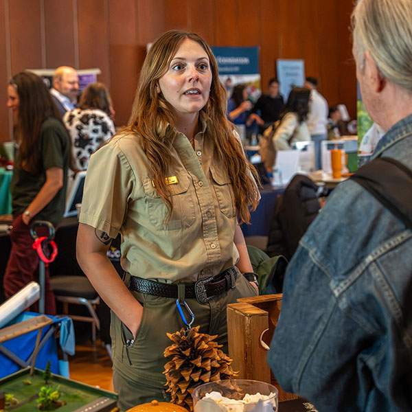 Woman in park ranger uniform speaking to partially obstructed man in crowded room