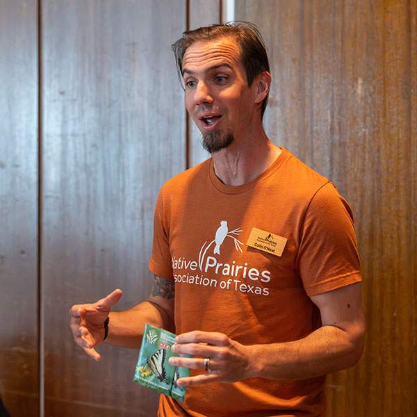 A man standing against a wall, speaking to someone off-screen