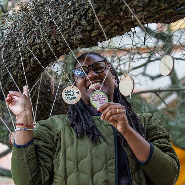 A girl standing under a tree, smiling while holding a circle tied to the branch