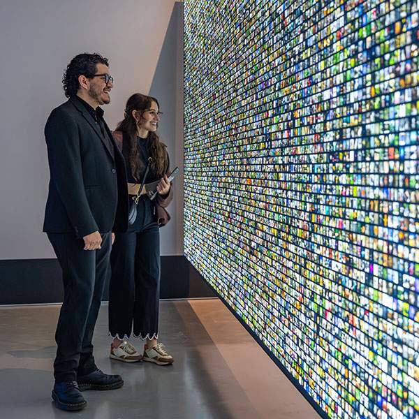 Two people look at wall of tiny, backlit square images