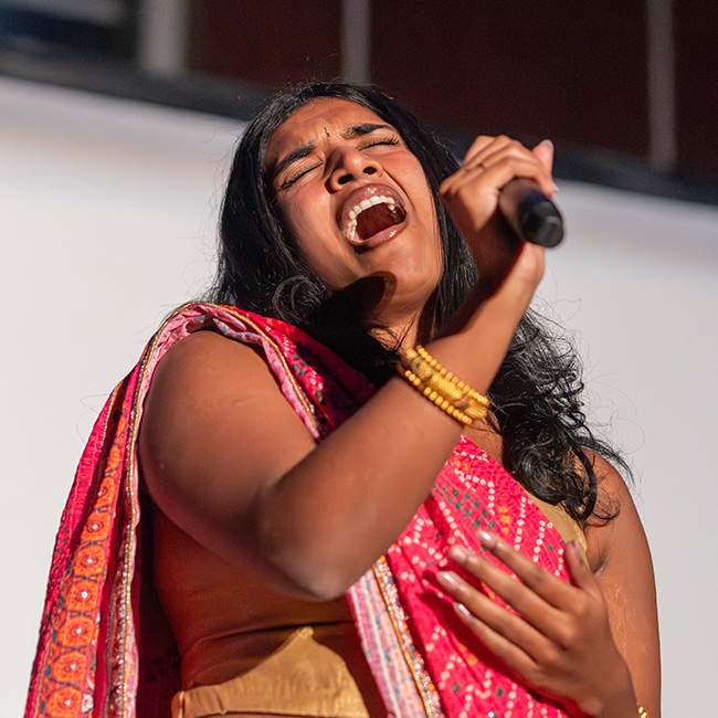 Girl singing, holding a mic away from her face as she hits a high note