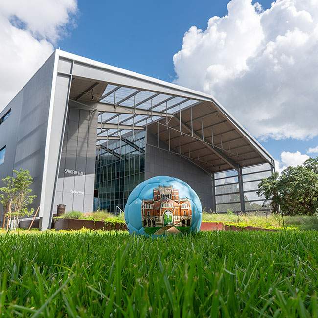Bugs-eye-view shot of a soccer ball on a grassy field, with a building in the background