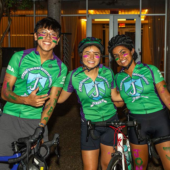 Three people in matching green shirts, wearing biking gear, pose together
